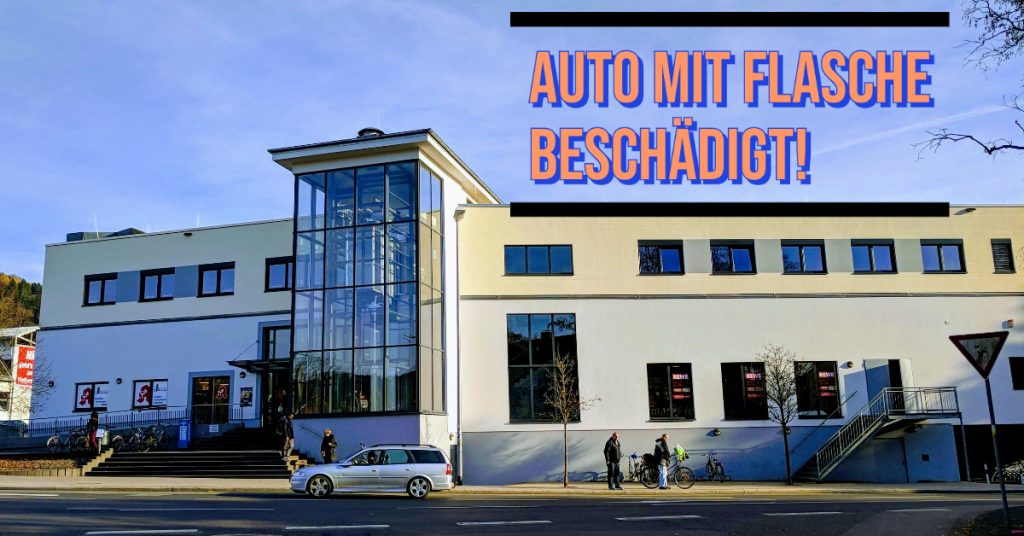 Auf dem Bild sieht man die Schrift Auto mit Flasche beschädigt. Zudem ist eine Szene vom Erlenring mit Auto und Straße zu sehen. 